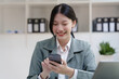 © NanSan - Pretty Asian business woman in black suit working at her office desk, with document file and paperwork. texting mobile smartphone or chat message