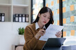 © NanSan - Cheerful asian businesswoman wearing sweater working at workplace female office worker during working day in office, working serious, looking at chart paper