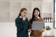 © NanSan - Cheerful asian business woman wearing sweater with colleagues working together at workplace female office worker during working day in office, looking laptop