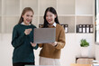 © NanSan - Cheerful asian business woman wearing sweater with colleagues working together at workplace female office worker during working day in office, looking laptop