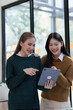 © NanSan - Cheerful asian business woman wearing sweater with colleagues working together at workplace female office worker during working day in office, looking tablet