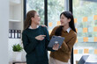 © NanSan - Cheerful asian business woman wearing sweater with colleagues working together at workplace female office worker during working day in office, looking tablet