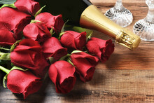  Valentines Day Or Love Concept. Closeup Of A Dozen Red Roses And A Bottle Of Champagne On A Wood Table.