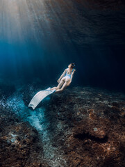 Wall Mural - Woman freediver glides underwater. Freediving with beautiful girl in deep ocean and amazing sun rays