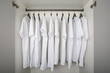 white t-shirts hang on a clothes rail in a white wardrobe. all t-shirts are the same color and size and are worn on hangers