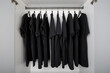 black t-shirts hang on a clothes rail in a white wardrobe. all t-shirts are the same color and size and are worn on hangers