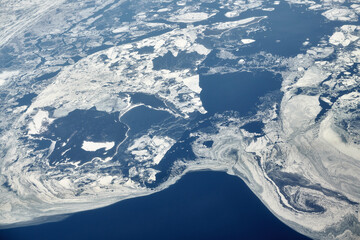 Aerial view from airplane window over clouds top to snow covered frozen sea, winter fresh frosty air. Beautiful hazed sky aerial view to Earth, snowy background texture