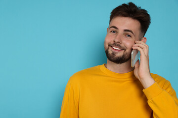 Wall Mural - Handsome man in yellow sweatshirt talking on phone against light blue background, space for text