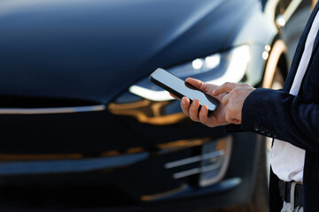 Unrecognizable elegant man using smartphone app for remote controlling of premium class Tesla Plaid car, driver distantly approaching car and opening door, smart car