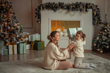 Happy New Year! family traditions. young mother and her daughter have fun at home near the Christmas tree and fireplace