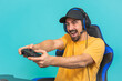 Excited young gamer man playing games holding joystick isolated on blue wall background studio portrait