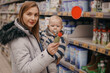 Young mother with baby son shopping in supermarket. A young mother chooses baby food with her baby sitting in a grocery cart. Close up. The concept of family shopping.