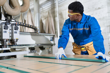 African American carpenter in safety uniform checking timber wood with machine at wood factory	