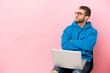 © luismolinero - Young man sitting on a chair with laptop making doubts gesture while lifting the shoulders