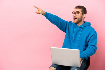 Poster - Young man sitting on a chair with laptop pointing away