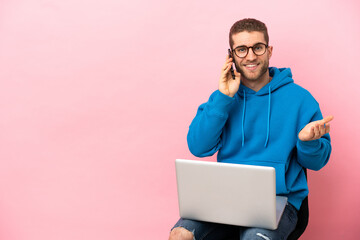 Poster - Young man sitting on a chair with laptop keeping a conversation with the mobile phone with someone