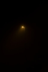 one single lamp standing and shining in the darkness with yellow light in the night on a street