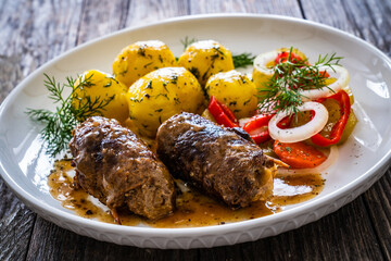 Wrapped pork in sauce served with boiled potatoes and vegetable salad on wooden table
