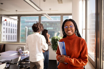 Black girl in office in foreground is looking at camera