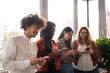 © jessica - Group of young people in the office, using phone during the break. Texting together in front of the window