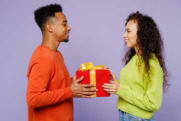 Wall Mural - Side view young couple two friend family man woman of African American ethnicity in casual clothes together give red present box with gift ribbon bow isolated on pastel plain light purple background