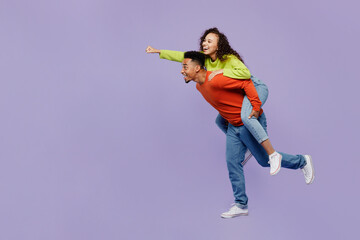 Poster - Full body side view young couple two friends family man woman of African American ethnicity in casual clothes together giving piggyback ride to joyful, sit on back isolated on plain purple background.