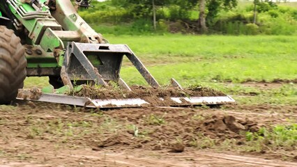 Wall Mural - Land work by the territory improvement. Small tractor with a ground leveler for moving soil, turf. A green mini skid steer loader clear the construction site. Machine for agriculture work. Copy space.