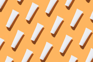 Pattern made with white tubes of sunscreen cream, hand cream or body lotion over orange background. Flat lay style, mockup image