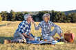 © pucko_ns - Mature couple sitting on blanket in nature and make picnic. She feed old man with piece of food and smile