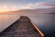 Long Exposure View Of A Pier On A Lake At Sunset, With Perfectly Still Water