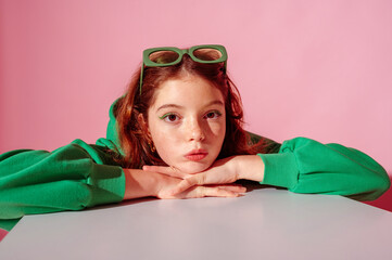 Beautiful freckled redhead girl wearing trendy green hoodie, posing against pink background. Close up studio portrait. Copy, empty space for text
