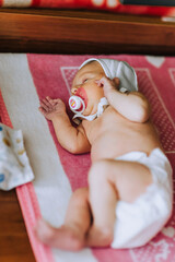 Wall Mural - A beautiful newborn baby, a little girl lies, sleeps in bed, with a pacifier in her mouth, eating on a blanket. Photography, childhood.