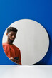 © Clique Images - Vertical creative studio mirror reflection portrait of handsome young Black man wearing coral sweater using his smart phone