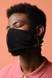© Clique Images - Vertical close-up portrait of unrecognizable stylish young African American man wearing black mask on face posing on camera with eyes closed against pink background