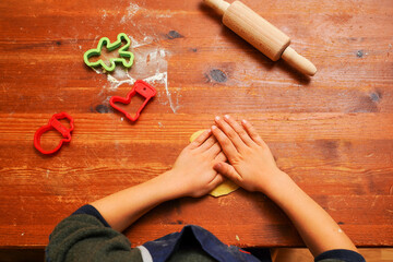 Hands of a toddler child cutting shaped biscuits out of dough on a brown wooden tabel. Christmas baking.