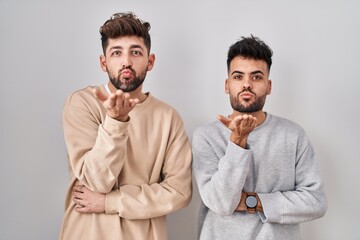 Wall Mural - Young homosexual couple standing over white background looking at the camera blowing a kiss with hand on air being lovely and sexy. love expression.