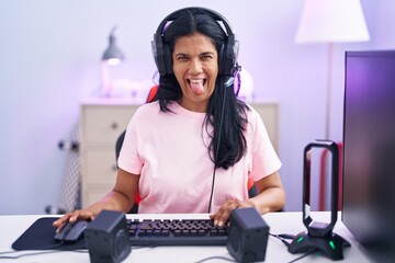 Poster - Mature hispanic woman playing video games at home sticking tongue out happy with funny expression. emotion concept.