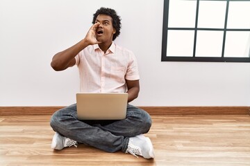 Wall Mural - African man with curly hair using laptop sitting on the floor shouting and screaming loud to side with hand on mouth. communication concept.