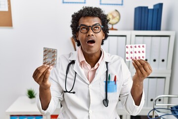 Poster - African man wearing doctor uniform holding prescription pills angry and mad screaming frustrated and furious, shouting with anger looking up.