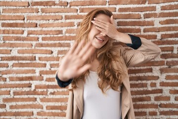 Canvas Print - Beautiful blonde woman standing over bricks wall covering eyes with hands and doing stop gesture with sad and fear expression. embarrassed and negative concept.