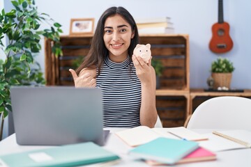 Wall Mural - Young teenager girl studying using computer laptop pointing thumb up to the side smiling happy with open mouth