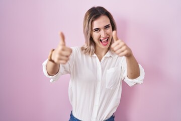 Poster - Young beautiful woman standing over pink background approving doing positive gesture with hand, thumbs up smiling and happy for success. winner gesture.