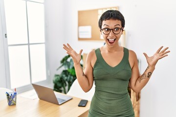 Sticker - Young hispanic woman with short hair working at the office celebrating victory with happy smile and winner expression with raised hands