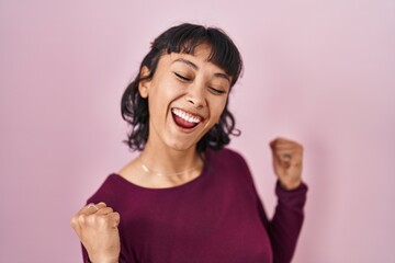 Sticker - Young beautiful woman standing over pink background very happy and excited doing winner gesture with arms raised, smiling and screaming for success. celebration concept.