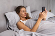 © F8  \ Suport Ukraine - Top view awakened woman lying in bed holds smart phone looks at screen watching time overslept and late feels stressed