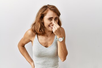 Wall Mural - Beautiful caucasian woman standing over isolated background smelling something stinky and disgusting, intolerable smell, holding breath with fingers on nose. bad smell