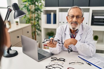 Wall Mural - Senior grey-haired man optician holding glasses showing to patient at clinic