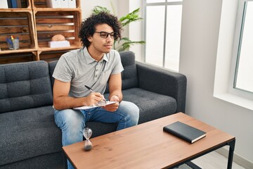 Poster - Young hispanic man psychologist writing on clipboard at psychology center