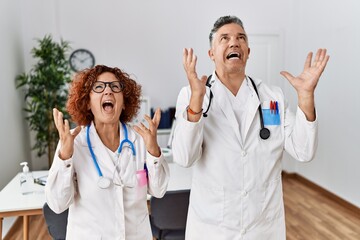 Sticker - Two middle age doctors at medical clinic crazy and mad shouting and yelling with aggressive expression and arms raised. frustration concept.