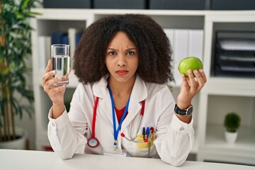 Poster - Young african american dietitian woman holding fresh apple and water skeptic and nervous, frowning upset because of problem. negative person.